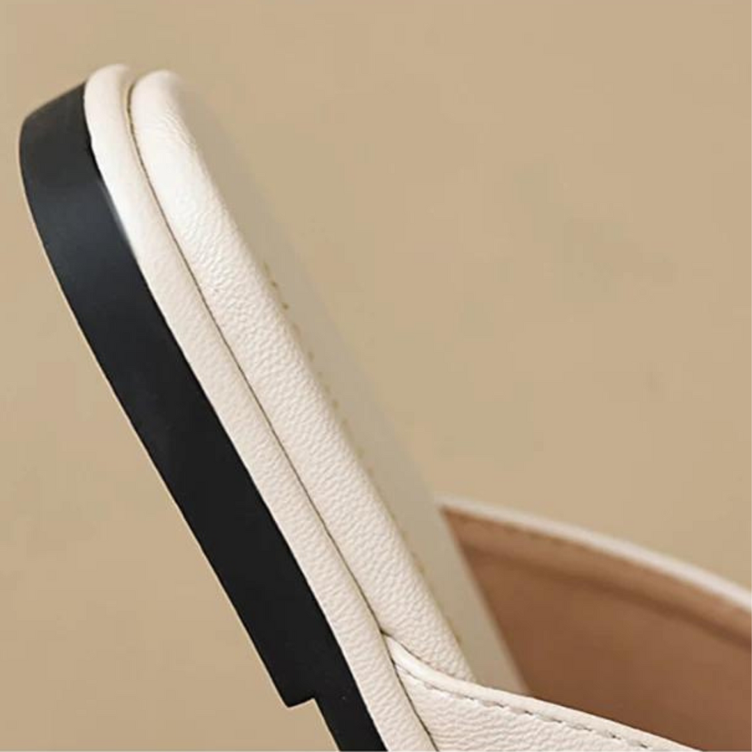 Close-up of the heel and sole of chic slides with a black outsole, highlighting texture and stitching details against a plain, light brown background—perfect for elevating your summer wardrobe.
