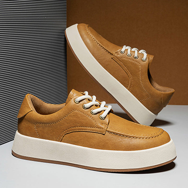 A pair of tan Men's Leather Casual Shoes with white laces and thick white soles are displayed against a modern, neutral-toned background. One breathable walking shoe stands upright while the other is propped up behind it.