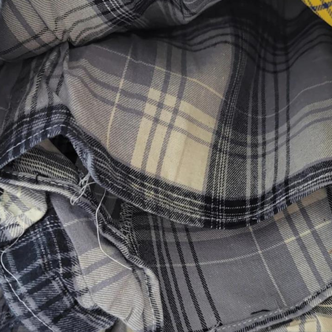 A close-up view of folded fabric with a black, gray, and beige plaid pattern. The material appears soft, with visible seams and some frayed edges—perfect for crafting an eclectic fashion piece like a patchwork skirt.