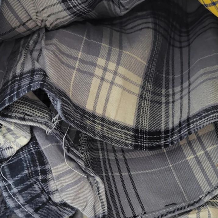 A close-up view of folded fabric with a black, gray, and beige plaid pattern. The material appears soft, with visible seams and some frayed edges—perfect for crafting an eclectic fashion piece like a patchwork skirt.