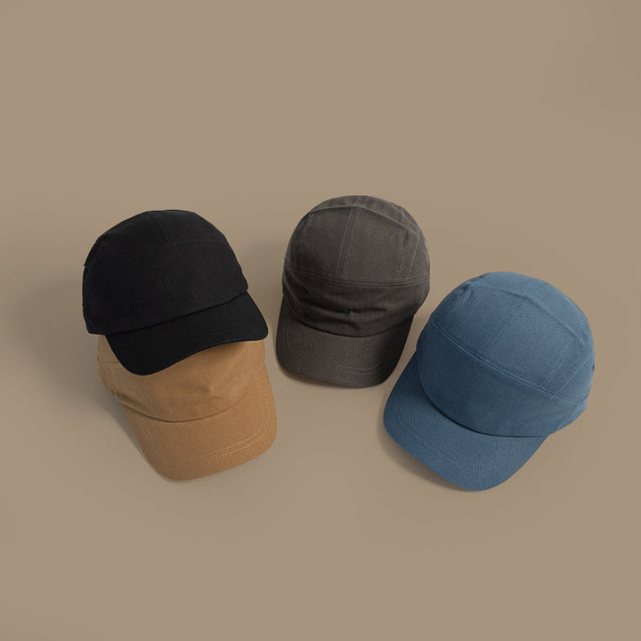 Four unisex caps in black, brown, gray, and blue—each a Japanese-style peaked cap with an adjustable strap—are arranged in a semi-circle on a plain beige background.