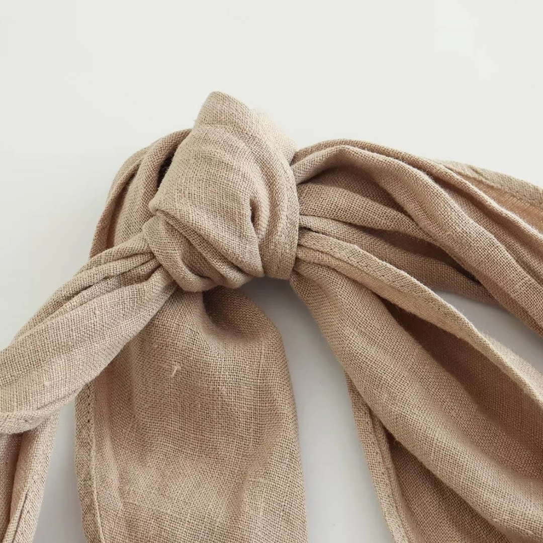 A close-up of a beige fabric scarf tied in a neat knot, its ends and loops draped loosely on a white background—a perfect accessory to elevate your summer style.