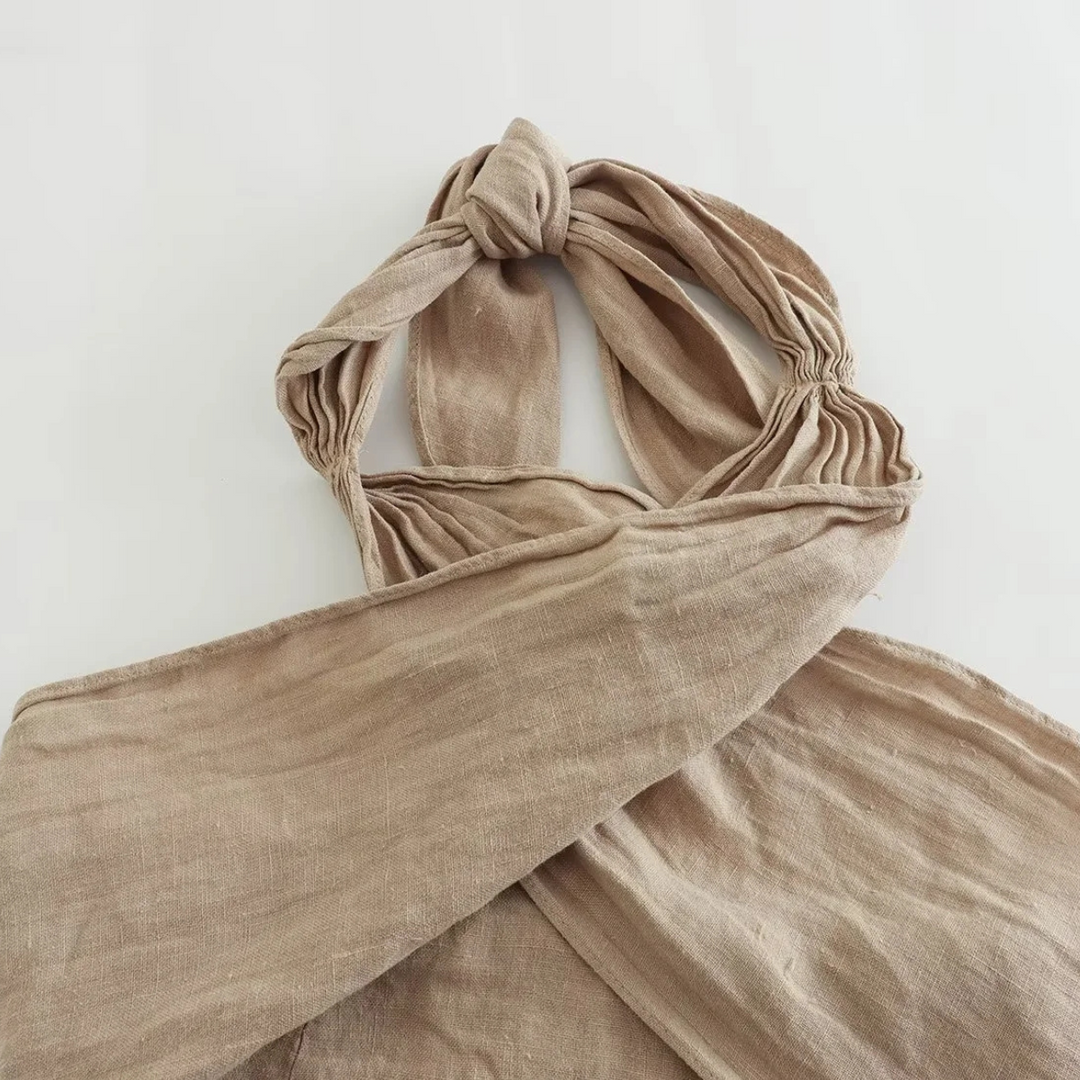A beige, crinkled fabric bag with a twisted, knotted handle lies flat on a white surface—its soft, unstructured look and earthy texture make it a perfect accessory for summer style.