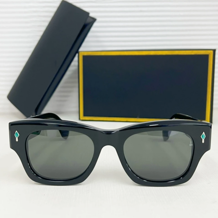 A pair of vintage-inspired black rectangular sunglasses with dark lenses is displayed in front of a black and gold-trimmed case and box. The frames feature small turquoise diamond-shaped accents and offer UV400 protection.