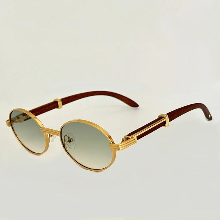 Vintage round sunglasses with gold metal frames, gradient grey lenses, and brown temples offer UV400 protection. A unique decorative metal detail accents the arms. The background is plain and light-colored.