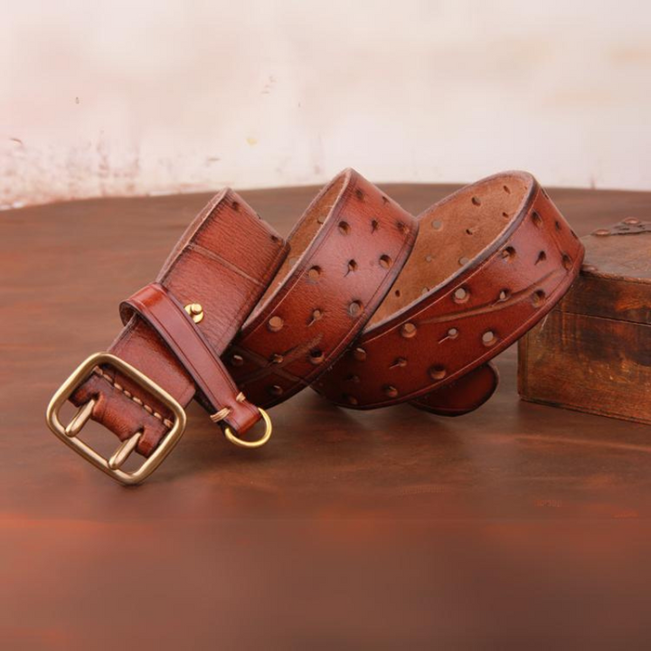 A handcrafted belt made from premium leather, featuring multiple small holes and a brass buckle, is displayed on a wooden surface next to a rustic wooden box.