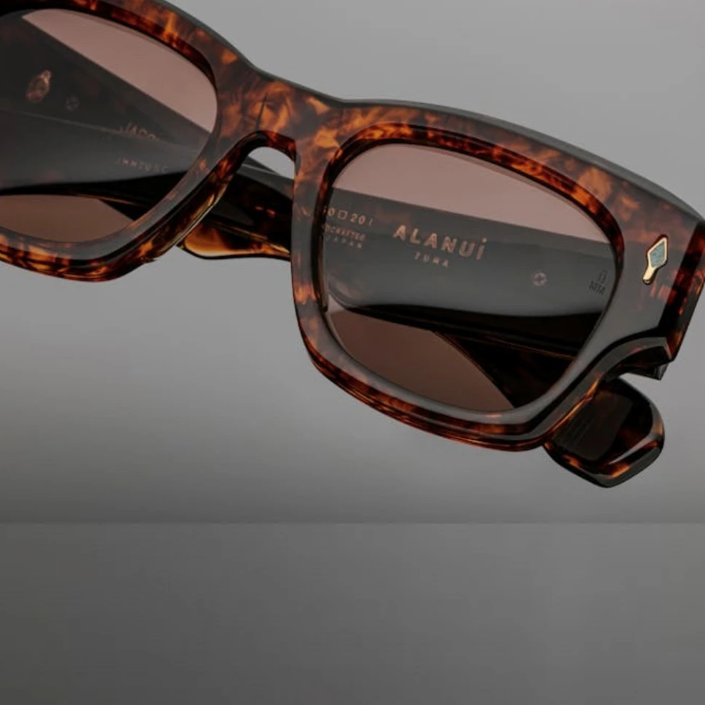Close-up of brown tortoiseshell square retro sunglasses with dark lenses and UV400 protection, featuring ALANUI branding on the inner arm, set against a plain grey background.