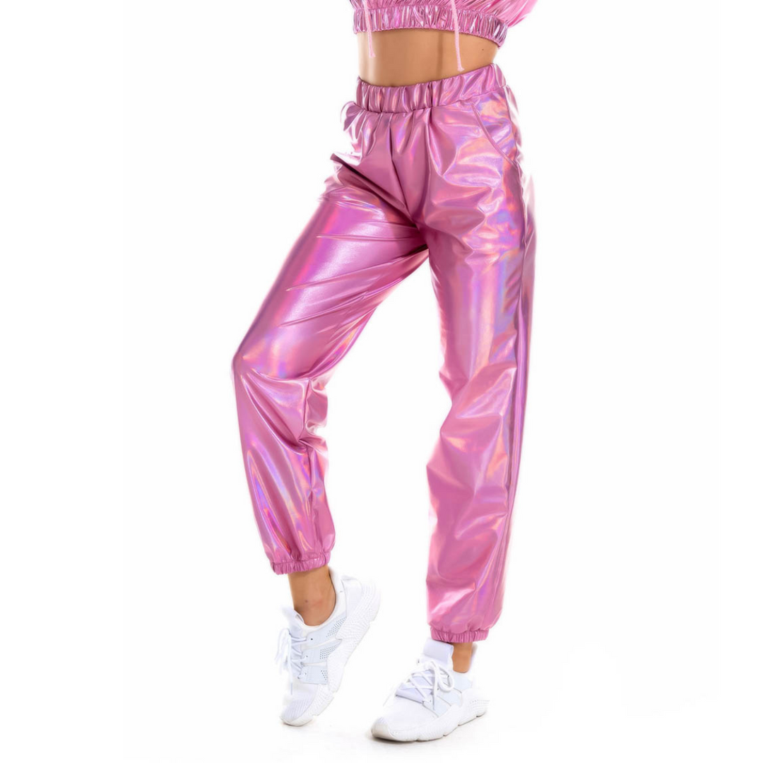A person wearing shiny, metallic pink jogger pants with a holographic finish and white sneakers, posing with one knee slightly bent against a white background.