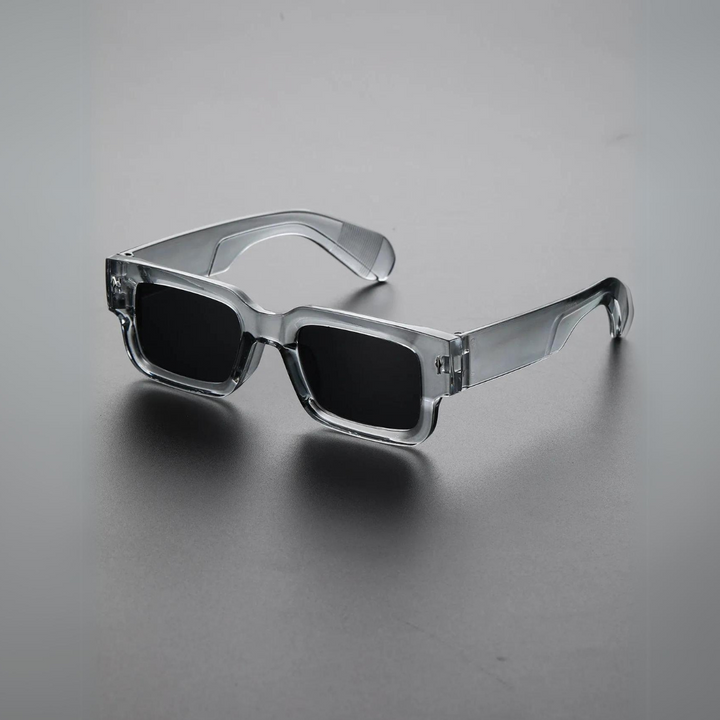 A pair of lightweight sunglasses with bold, angular, transparent grey frames and dark UV400 protection lenses, displayed on a smooth grey surface.