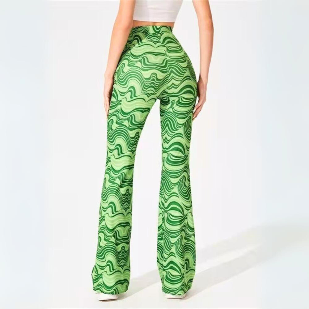 A person wearing high-waisted, psychedelic flare pants with a wavy green pattern stands facing away from the camera. They pair these trendy statement pants with a white crop top against a plain, light-colored background.