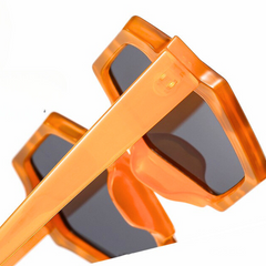 Close-up of trend-forward orange sunglasses with dark lenses and a bold hexagonal frame, shown against a white background. These stylish sunglasses offer UV400 protection and feature thick, angled frames for a modern look.