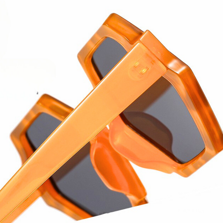 Close-up of trend-forward orange sunglasses with dark lenses and a bold hexagonal frame, shown against a white background. These stylish sunglasses offer UV400 protection and feature thick, angled frames for a modern look.