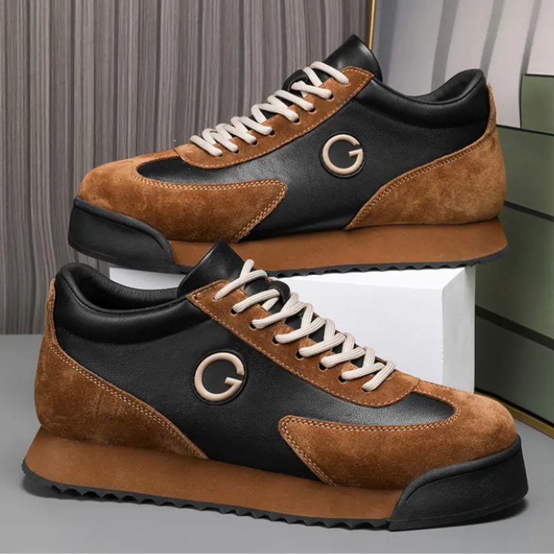 A pair of sleek sneakers with luxe leather suede in brown and black panels, white laces, and a circular G logo on the side, displayed against a modern, neutral background. Perfect for the urban professional.