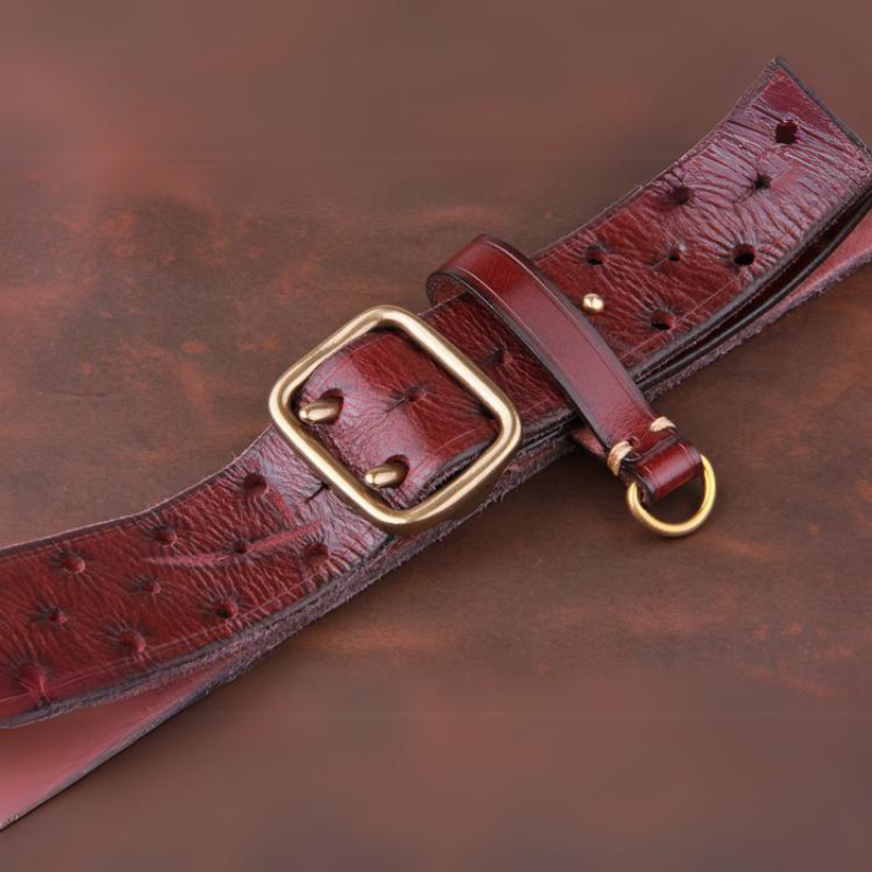 A wide, textured vintage leather belt with a rectangular gold buckle and gold ring, lying flat on a matching brown surface.