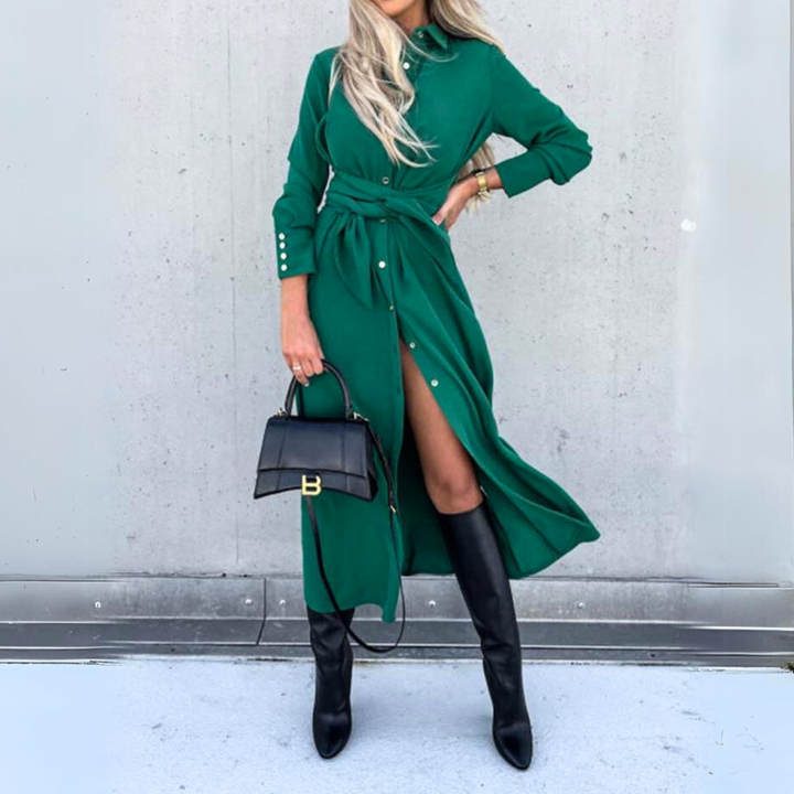 A woman in a long-sleeve wrap dress with a belt poses against a gray wall, holding a black handbag and wearing knee-high black boots, channeling effortless high fashion. Her face is not visible.