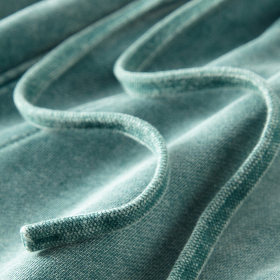 A close-up of a teal-colored sweatshirt drawstring resting on matching sweatshirt fabric, highlighting the texture and soft material of both the cord and the garment, along with tapered cuffs for added comfort.