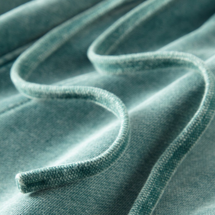 A close-up of a teal-colored sweatshirt drawstring resting on matching sweatshirt fabric, highlighting the texture and soft material of both the cord and the garment, along with tapered cuffs for added comfort.