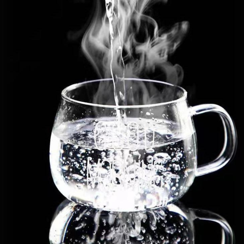 Clear heat-resistant glass mug on a black background with hot water being poured in, creating steam and bubbles inside the cup.