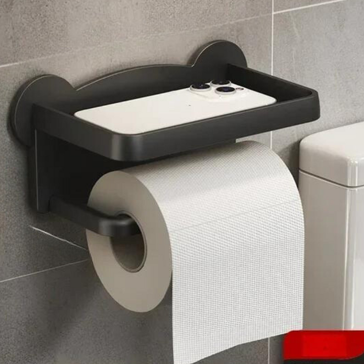 A wall-mounted black toilet paper holder with a moisture-resistant, multi-functional shelf for your smartphone, installed on a gray tiled bathroom wall next to a white toilet.