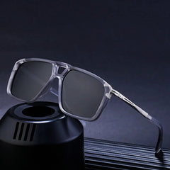 A pair of square, translucent gray polarized sunglasses with dark lenses is displayed, resting on a black cylindrical stand against a dark background.