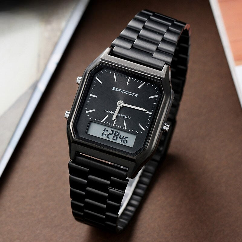 A black SANDA Luxury G Style Watch with a metal strap features a dual display—both analog and digital—set against a brown surface with parts of a white paper and book visible in the background.