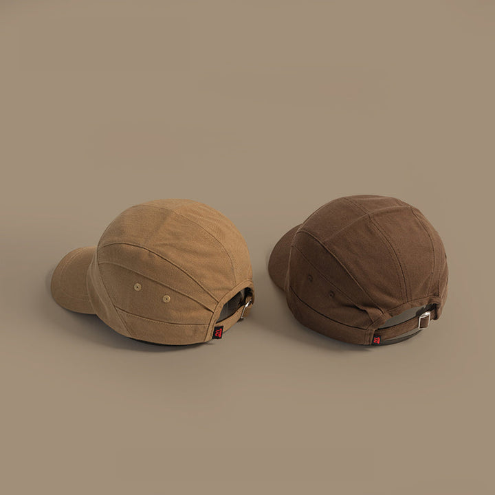 Two unisex caps in tan and dark brown are displayed on a neutral background, shown from the back to highlight the adjustable strap and metal buckles.