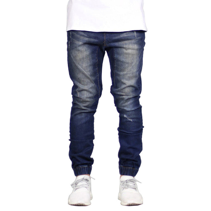 A person wearing dark blue, straight tapered leg, jogger-style jeans with faded details, paired with a white shirt and white sneakers. Only the lower half of the body is visible, giving off a subtle vintage aesthetic.