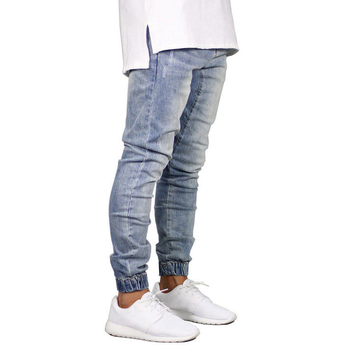 A person in light blue straight tapered leg jogger pants, a white shirt, and white sneakers stands against a plain white background. The image is cropped above the waist, giving off a modern twist on the vintage aesthetic.