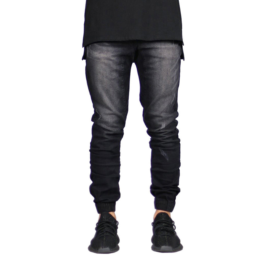 A person wears black jogger jeans with a faded effect and straight tapered leg, paired with a long black shirt and black sneakers. The image is cropped above the shoulders, highlighting a modern look with vintage aesthetic.