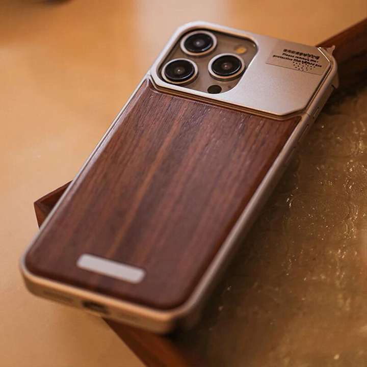 A smartphone with a triple camera setup features a stylish phone case with a silver metallic edge and a wood grain back, resting on a textured surface near a wooden tray.