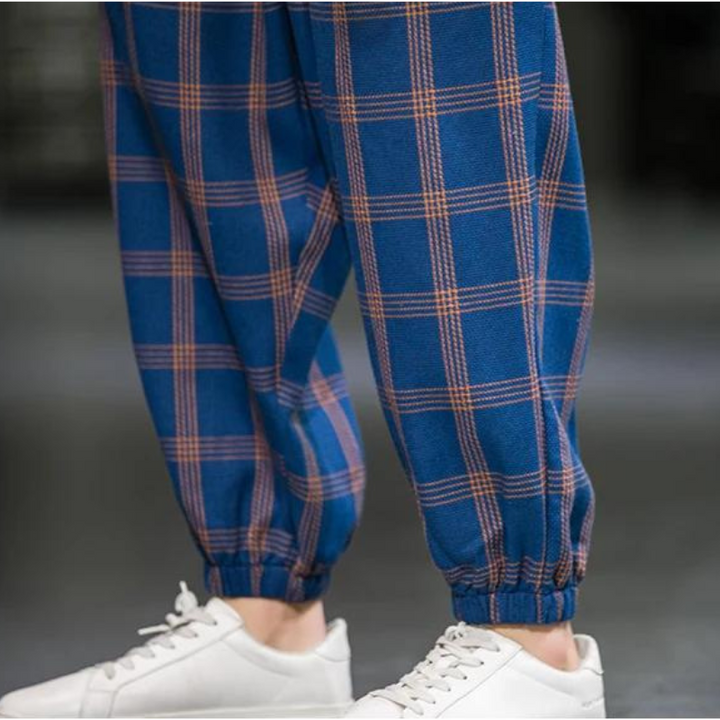 A person wearing blue plaid cotton joggers with orange lines and white sneakers; the elastic cuffs add a touch of Tokyo streetwear. The background is blurred.