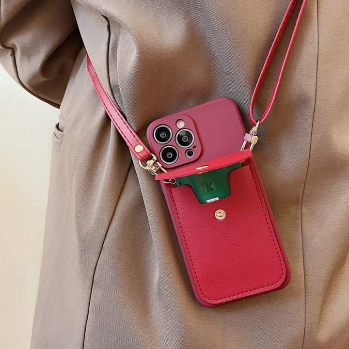 A person wearing a tan jacket carries a smartphone in a red phone case wallet with a secure cardholder and front pocket holding a green item. The case, featuring three cameras, includes a leather detachable strap for convenience.