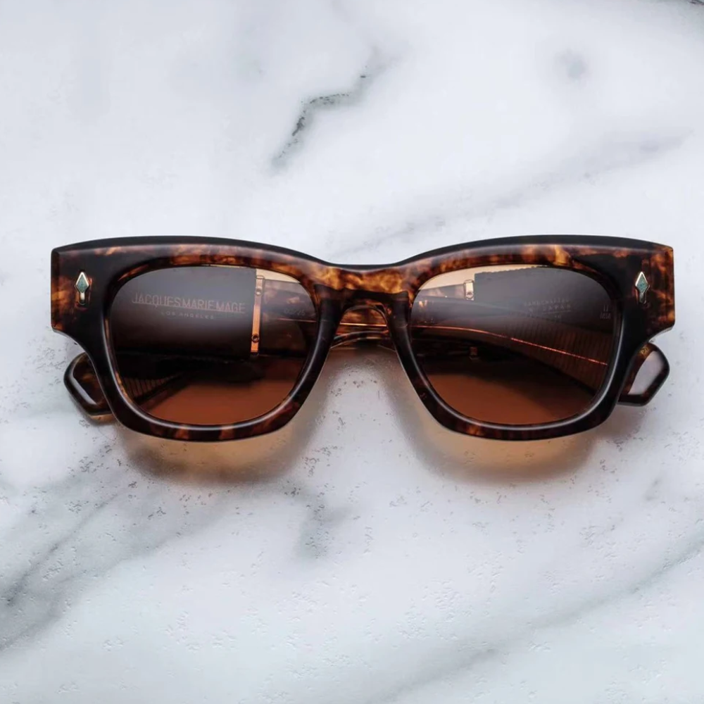 A pair of vintage-inspired tortoiseshell sunglasses with rectangular frames and brown tinted lenses rests on a white marble surface.