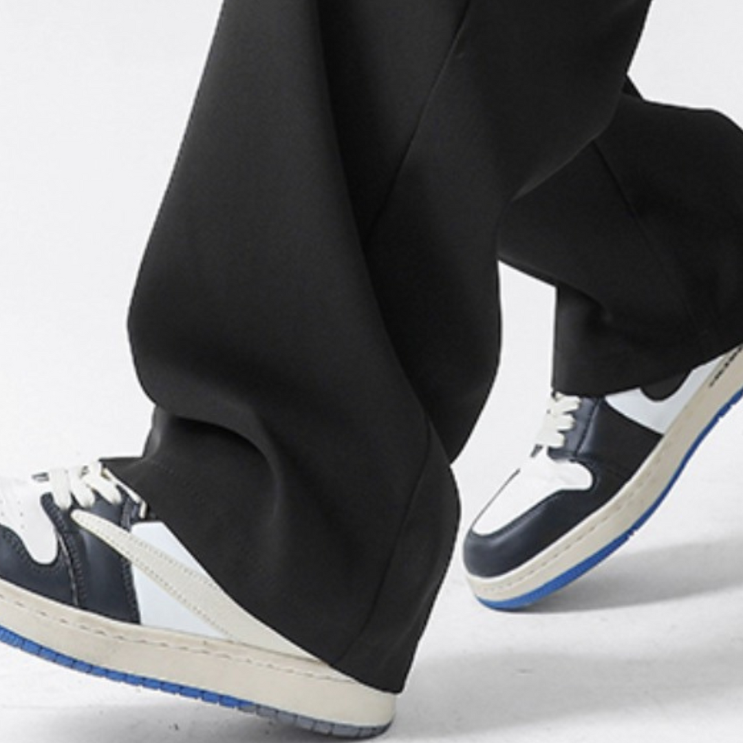 A person wearing black GOAT Joggers and black-and-white sneakers with blue soles is walking, with the streetwear joggers slightly covering the shoes.