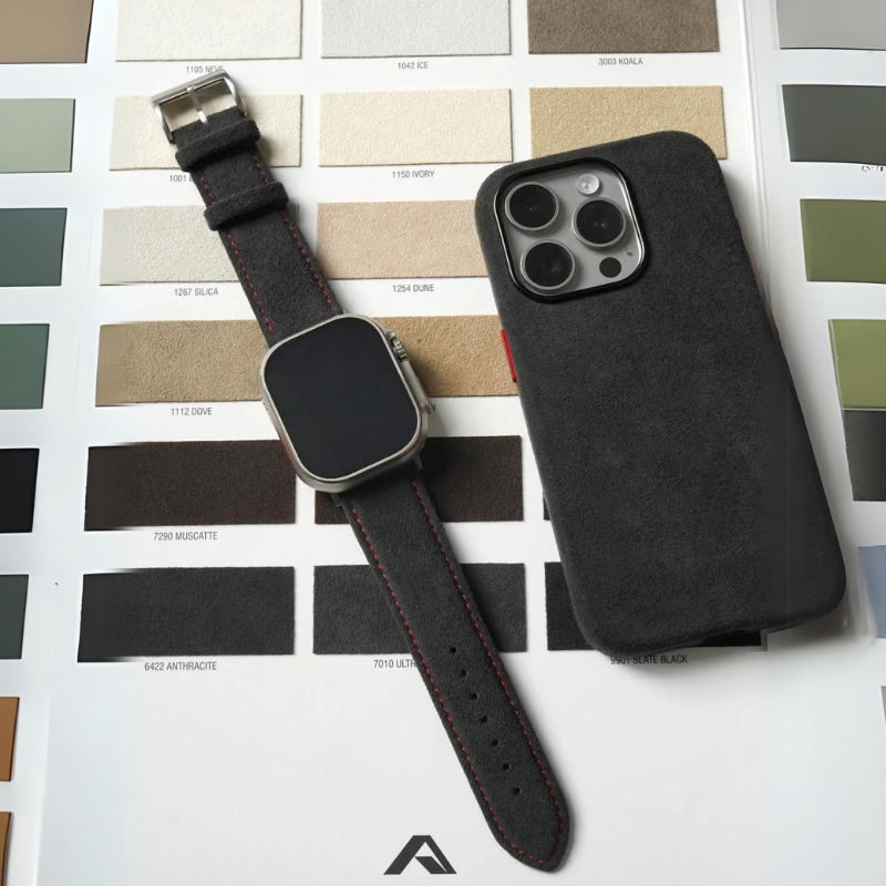 A smartwatch with a precision fit black band and a smartphone in a black case are placed on top of a color swatch chart featuring various shades of neutral and earthy tones.