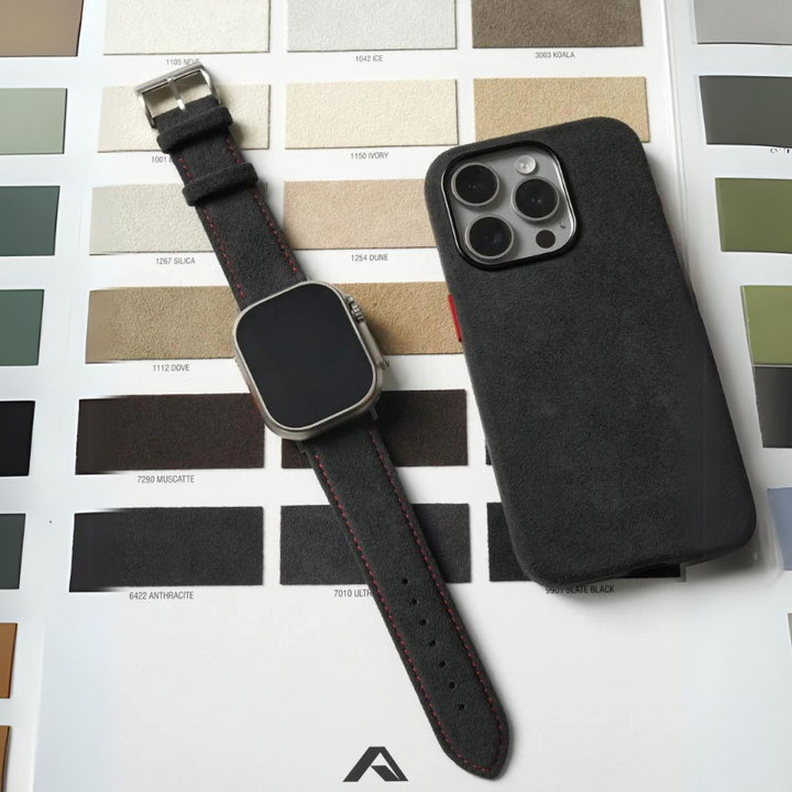 A smartwatch with a precision fit black band and a smartphone in a black case are placed on top of a color swatch chart featuring various shades of neutral and earthy tones.
