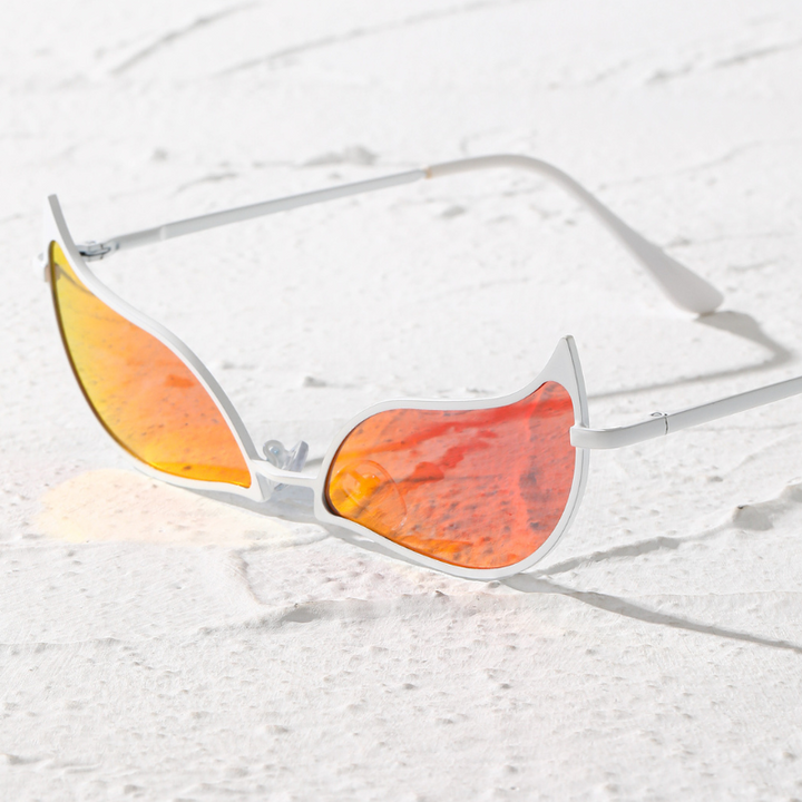 White-framed sunglasses with orange-tinted, flame-shaped lenses and a lightweight frame rest on a textured white surface, casting a shadow.