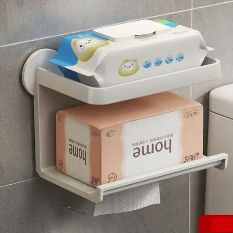 A moisture-resistant, wall-mounted bathroom shelf holds wet wipes on top and a pink tissue box below, with a tissue partially pulled out. The shelf is installed on a tiled wall next to the toilet.