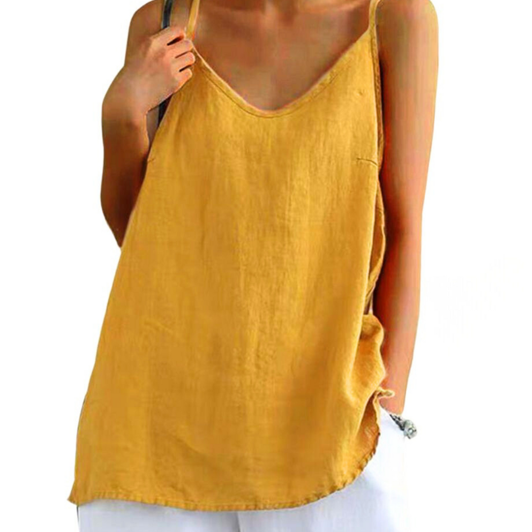 A person wears a loose, urban-chic camisole in yellow with thin straps and white pants. One hand holds a strap, while the other rests in their pocket. The plain white background highlights this effortless streetwear style.