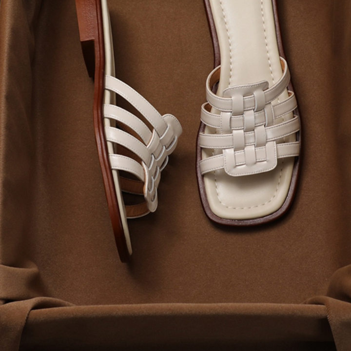 A pair of white woven Italian leather strappy sandals with square-toe design and brown soles, displayed on a soft brown fabric background.