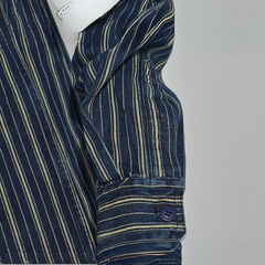 A close-up of a relaxed-fit button-down navy shirt sleeve with thin yellow and white vertical stripes, showing a buttoned cuff. The sleeve is partially folded, and a white object is tucked under the arm.