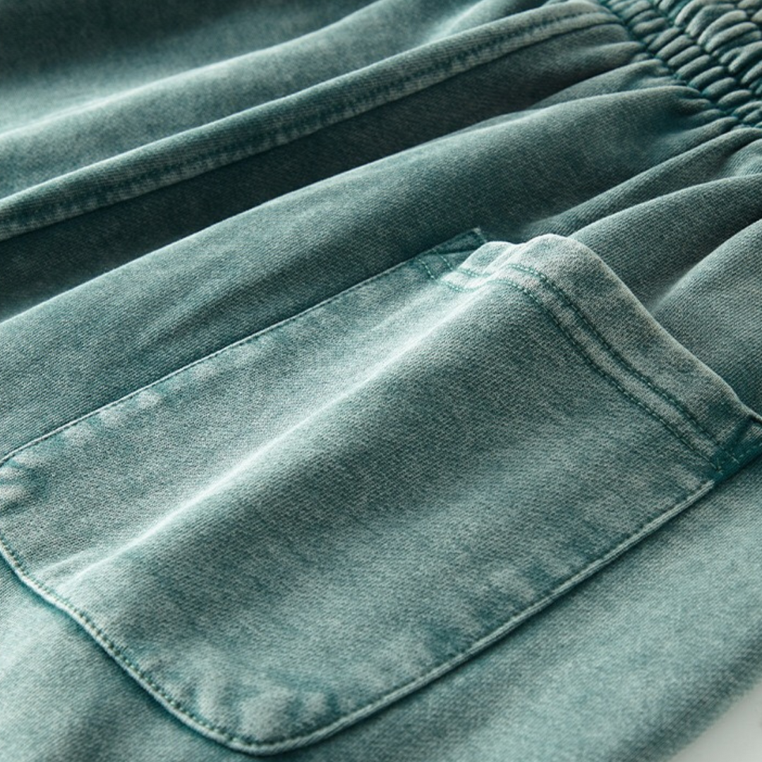 Close-up of a teal green garment with deep pockets and an elastic waistband, featuring soft, slightly faded fabric and a visible pocket detail.