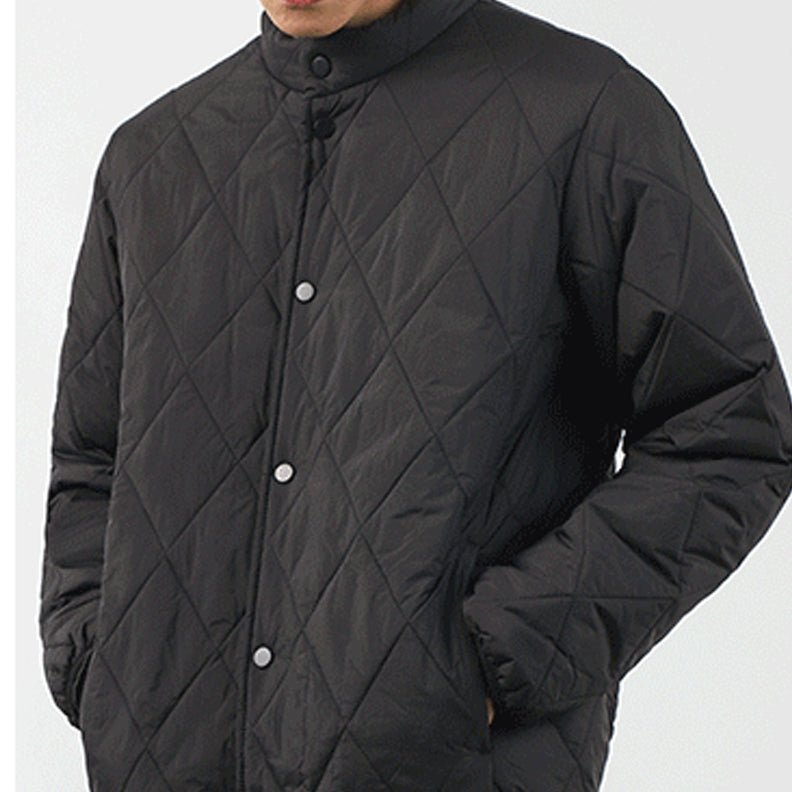 A person wearing a black, diamond-stitched pattern padded jacket with snap buttons stands against a plain light background. The lightweight insulating jacket features hands in pockets, and the head is partially out of frame.