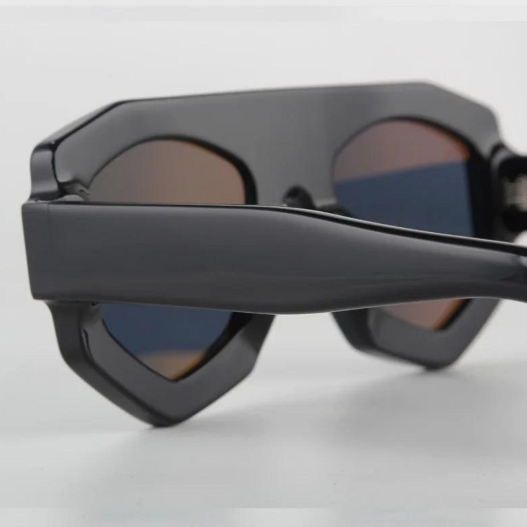 Close-up of black acetate geometric sunglasses with thick frames and dark, slightly reflective lenses, offering UV400 protection while resting on a white surface.