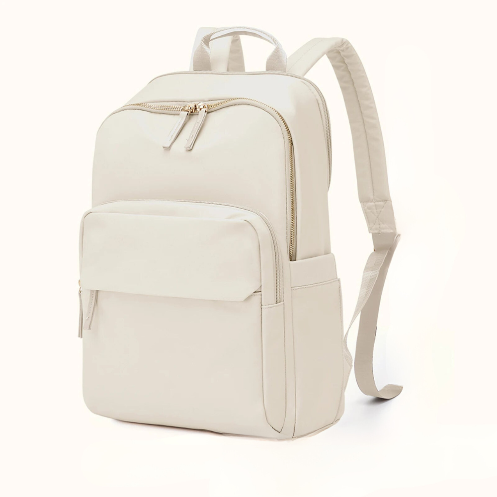 A minimalist, light beige, water-resistant backpack with gold zippers, a large front pocket, side pockets, adjustable padded shoulder straps, and a dedicated laptop compartment, displayed against a plain white background.