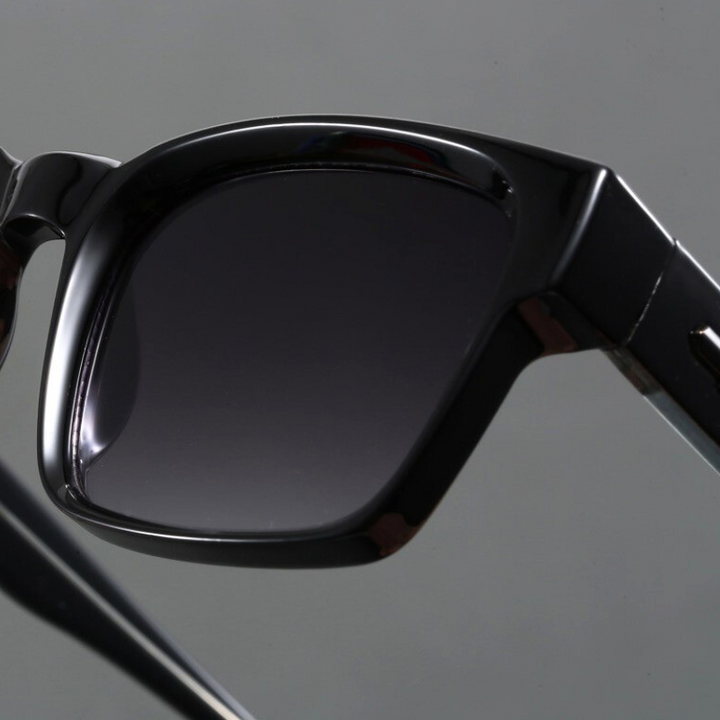 A close-up of a pair of black sunglasses with dark tinted lenses and modern design, shown against a plain gray background.