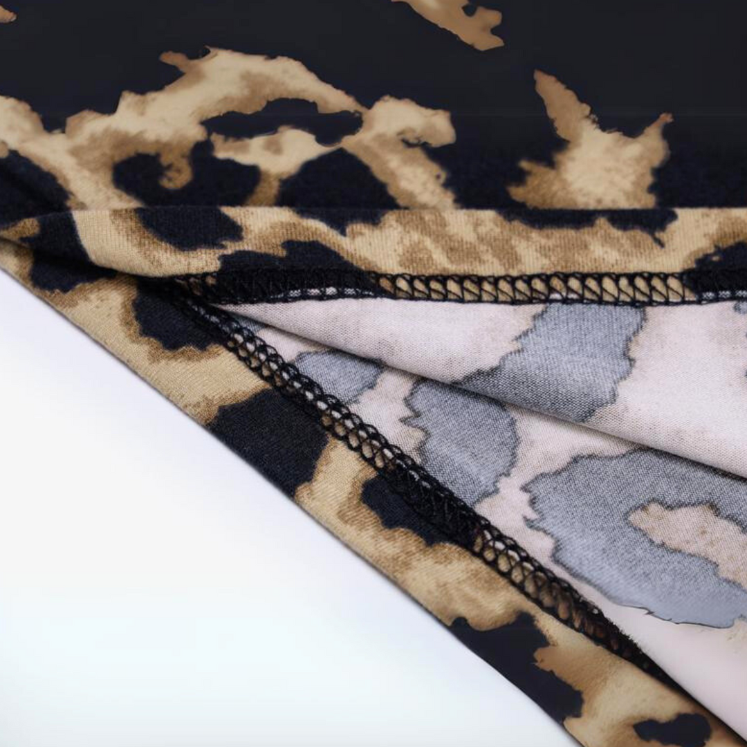 Close-up of overlapping fabric pieces with brown, black, and beige leopard print dress pattern. The edges are stitched with black thread, showing both the printed outer and lighter inner sides of this animal print dress fabric.