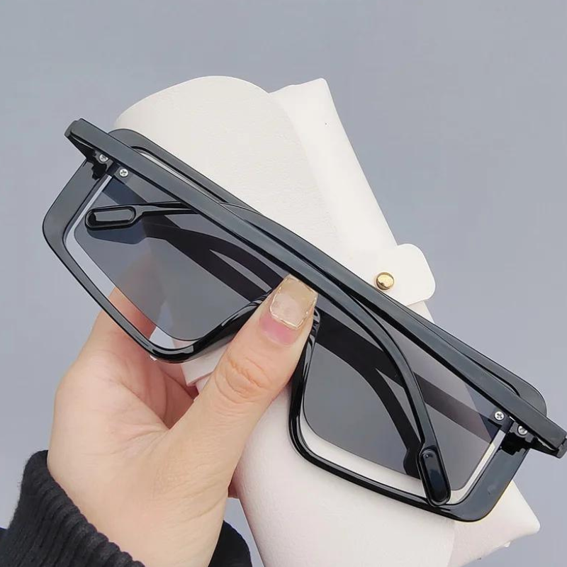 A hand holding black rectangular sunglasses with UV400 lens and gradient lenses, positioned in front of a white, textured eyeglasses case against a plain grey background.