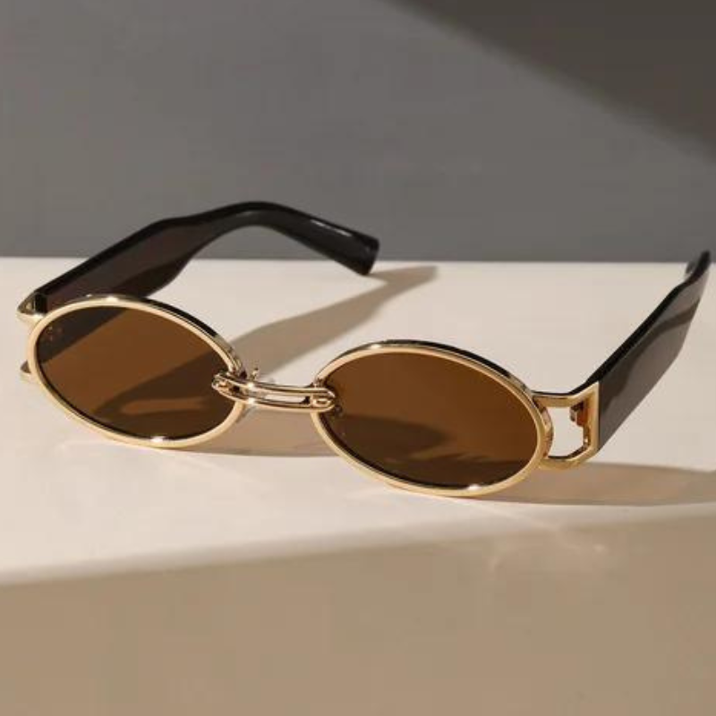 A pair of stylish retro oval sunglasses with a durable metal frame, gold accents, and brown lenses featuring thick black arms, resting on a white surface against a gray background.