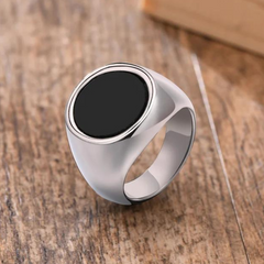 A silver signet ring with a large, flat black circular stone and a polished finish is displayed on a wooden surface, perfect for versatile styling.